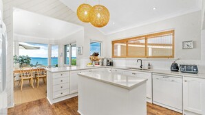 Eine moderne Küche mit einer großen Kochinsel, weißen Schränken und Blick aufs Meer.