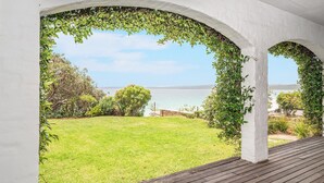 Eine überdachte Terrasse mit Blick auf eine Rasenfläche und ein Gewässer.