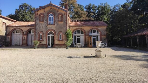 Ein historisches Gebäude mit einer symmetrischen Fassade, Bogenfenstern und einem Kieshof.