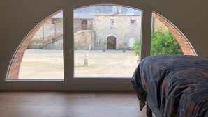 Ein Zimmer mit einem Bett und einem großen Bogenfenster mit Blick auf einen Innenhof, auf dem sich ein Gebäude und eine Treppe befinden.