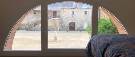 Una habitación con una cama y un amplio ventanal de arco que da a un patio con un edificio y una escalera.