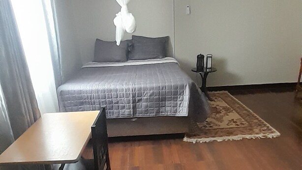 A room with a bed, a table, and chairs. - Furnished Self Catering cottage (Lusaka)