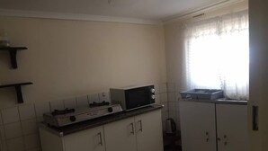 A small kitchen with white cabinets, a microwave, and a sink. - Furnished Self Catering cottage (Lusaka)