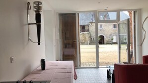 A room with a bed, a red chair, a table, and a large window with a view of a courtyard and old buildings. - Château du Parc Soubise - Gîte Parthenay l'Archevêque (Mouchamps)