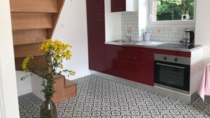 A kitchen with red cabinets, a white countertop, and a window with a view of trees. - Château du Parc Soubise - Gîte Parthenay l'Archevêque (Mouchamps)