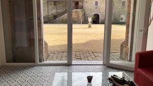A room with a glass coffee table, a red chair, and a view of a courtyard with a stone building and a fountain. - Château du Parc Soubise - Gîte Parthenay l'Archevêque (Mouchamps)