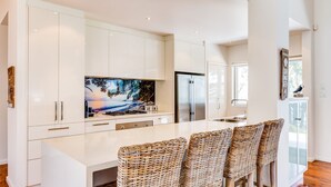 A modern kitchen with white cabinetry, a large island with bar stools, and a painting above the island.