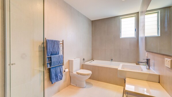 Une salle de bain moderne équipée d’une baignoire, de toilettes et d’une douche à parois de verre.