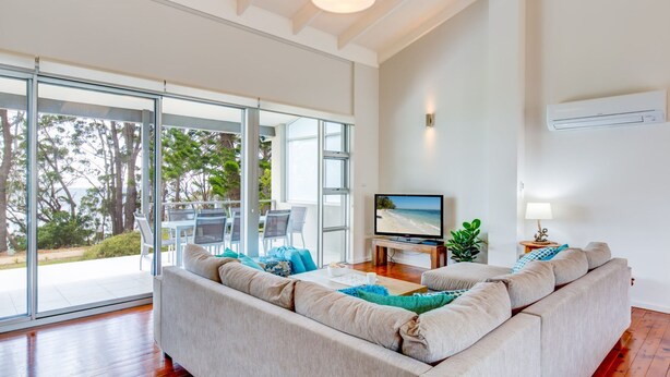 A modern living room with a large sofa, a television, and a dining area with chairs and a table.