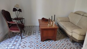 A living room with a patterned floor, a wooden side table with candles, a red chair, a beige sofa, and a lamp. - Château du Parc Soubise - Gîte Bonfils (Mouchamps)