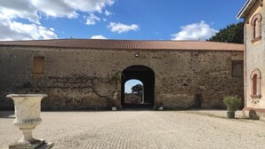 A courtyard with a large stone building featuring an arched entrance, a small window, and a potted plant. - Château du Parc Soubise - Gîte Bonfils (Mouchamps)