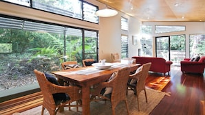 Amplia habitación con una gran mesa de comedor, sillas de mimbre, un sofá rojo y ventanas amplias con vistas al exterior.