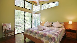 Un dormitorio con cama, una silla, una mesita de noche y un ventilador de techo.