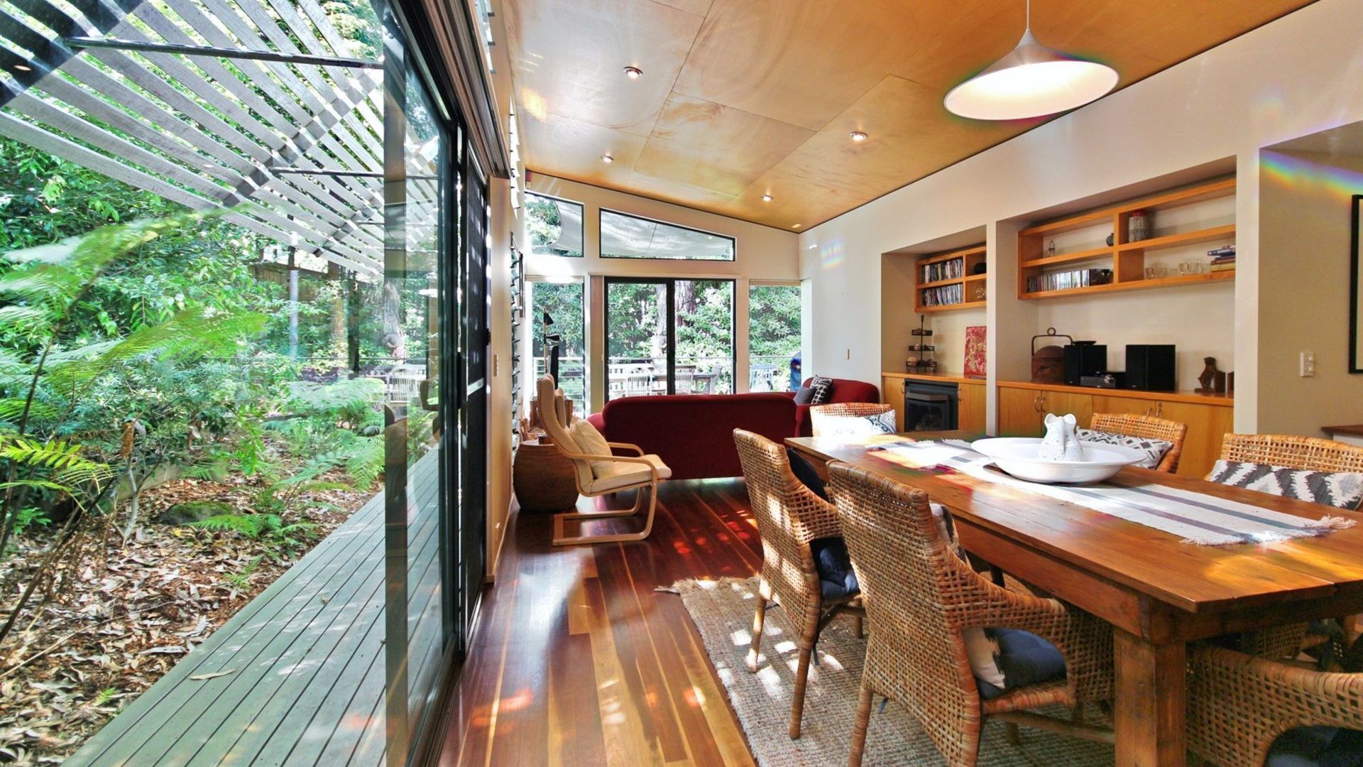 A modern interior with a dining area, wicker furniture, and a view of a lush garden.