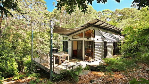Una cabaña moderna con terraza, ventanas amplias y vistas al bosque circundante.