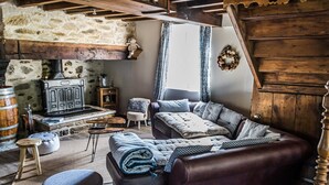 A rustic living room with a stone wall, wooden beams, a fireplace, a sofa, and a coffee table. - Au nid de Caroline (ISSOR)