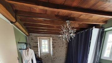 A bedroom with a wooden ceiling, a bed with a floral duvet, a small rug, and a hanging chandelier.