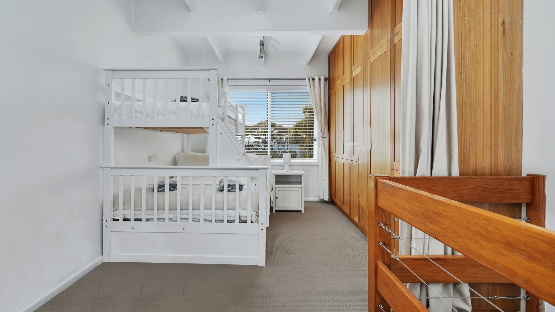 Une chambre avec des lits superposés, un petit bureau et une fenêtre avec des stores.