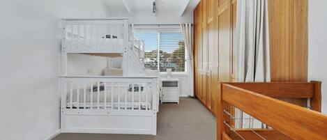 Une chambre avec des lits superposés, un petit bureau et une fenêtre avec des stores.