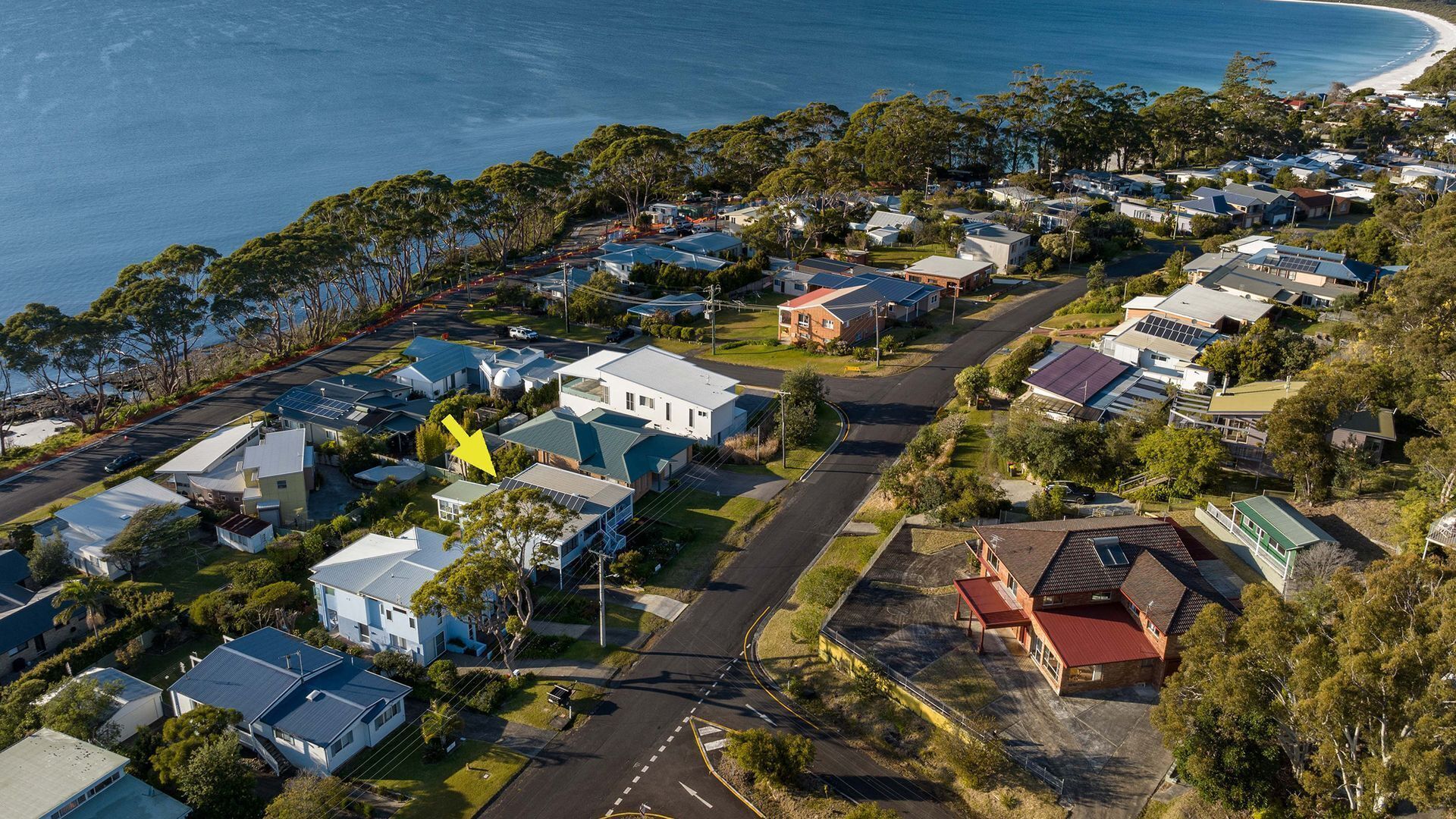 An aerial view of a coastal residential area with houses, roads, and a beach.