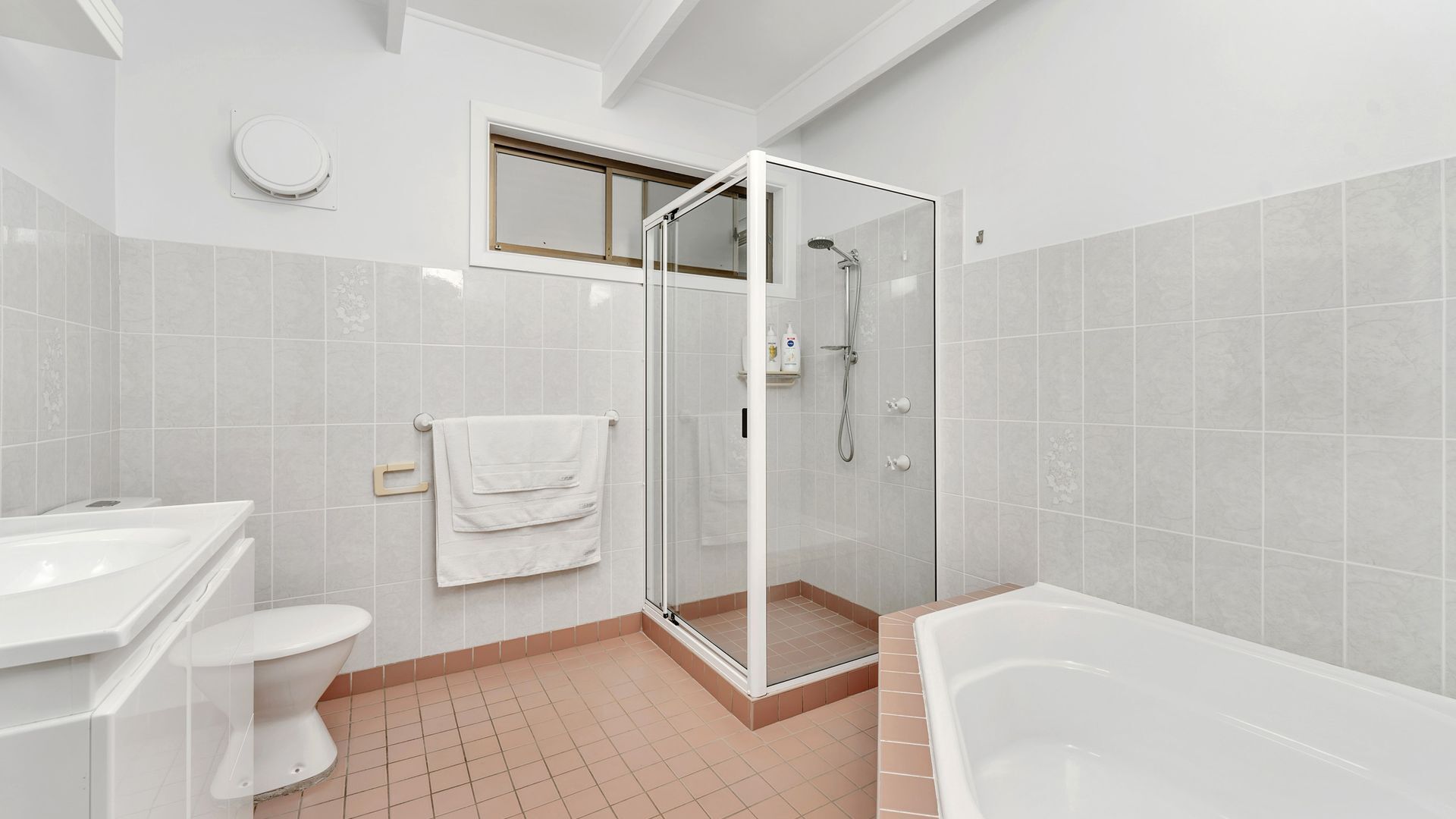 A modern bathroom with a glass-enclosed shower, a white bathtub, and a toilet.