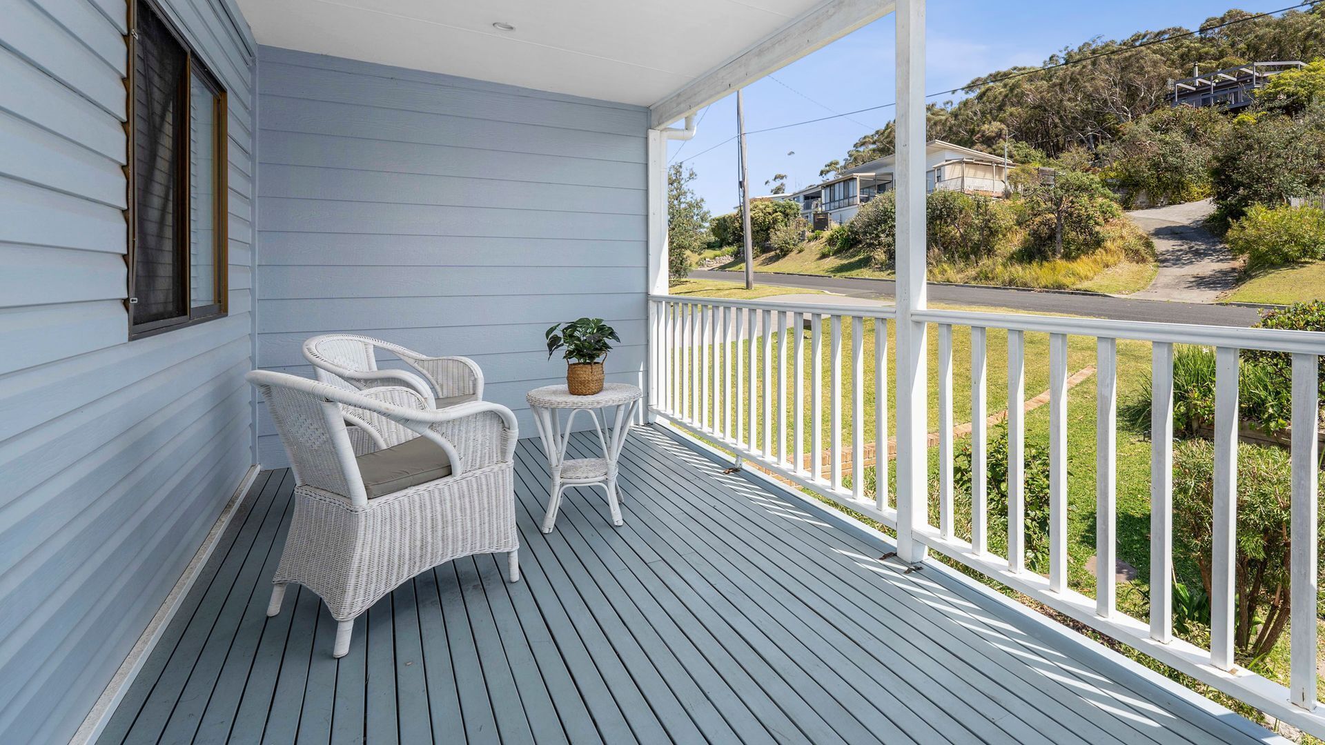 A covered porch with a white wicker chair and a small table, overlooking a residential street.