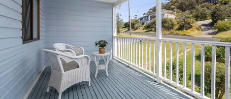 A covered porch with a white wicker chair and a small table, overlooking a residential street.