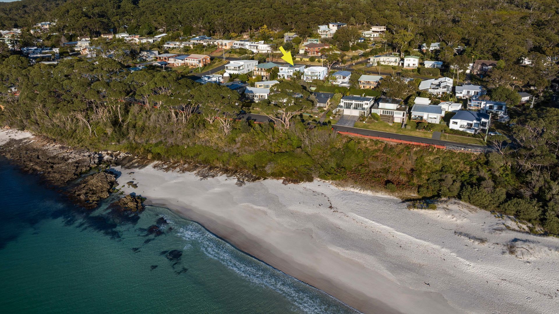 Oversigtsbillede af et kystnære boligområde med huse, en strand og en vej.