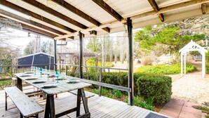 Eine Terrassengruppe mit Holztisch, gedeckt für ein Essen, umgeben von einer Holzterrasse und einem überdachten Bereich mit Blick auf einen Garten und Bäume.