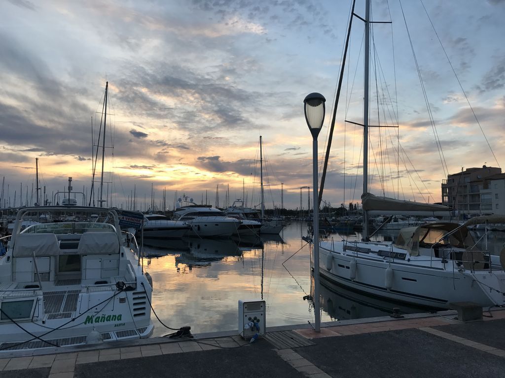 A marina with multiple boats docked, a lamppost, and a building in the background.