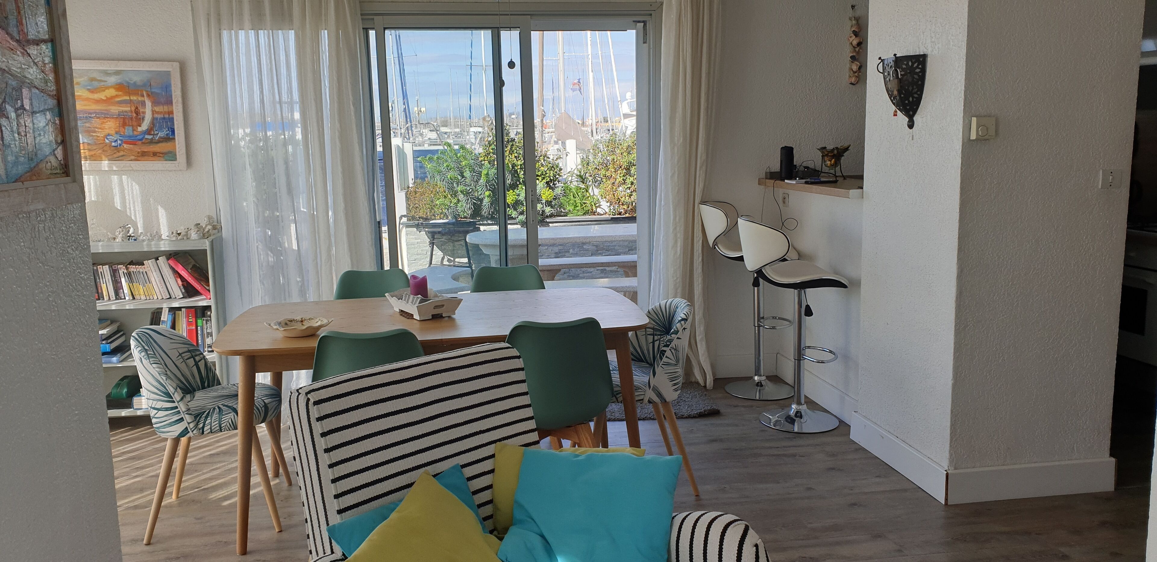 A dining area with a table, chairs, and a view of boats through large windows.