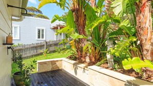 Une terrasse en bois agrémentée d’un jardinier en pierre, entourée de plantes tropicales et d’une clôture en bois.