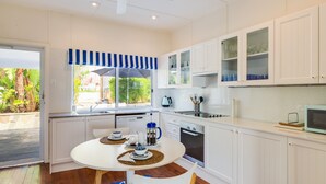 Une cuisine moderne avec des meubles blancs, une table à manger avec des sets de table et une fenêtre surmontée d’un auvent à rayures bleues.