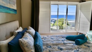 Une chambre à coucher avec un lit, des oreillers et une vue sur la mer par la fenêtre.