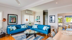 Un salon moderne avec un canapé d’angle bleu, une table basse en verre et un coin repas comprenant une table et des chaises blanches.