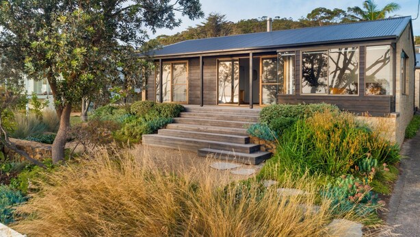 Una casa moderna con fachada de madera, amplias ventanas y una escalera de piedra que conduce a la entrada.