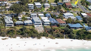 Vista aérea de una zona residencial costera con casas modernas, una playa de arena y gente disfrutando.