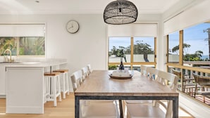 Una cocina moderna con muebles blancos, una mesa de comedor de madera y un amplio ventanal con vistas a un jardín.