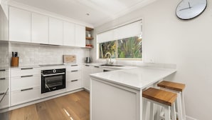 Una cocina moderna con armarios blancos, horno empotrado, pileta y ventana con vista a follaje.