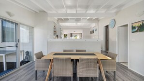 A modern dining area with a wooden table and wicker chairs, a glass door leading outside, and a clock on the wall.