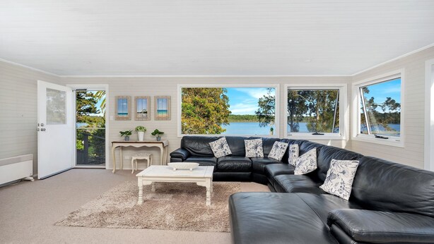 A spacious living room with a black leather sofa, a white coffee table, and a view of a lake through large windows.