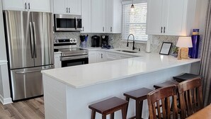 A modern kitchen with white cabinets, stainless steel appliances, a central island with stools, and a dining table. - Beautiful Lake Front in Quiet Cove, Convenient to Boat Ramp, Dining & Shopping (Henrico)