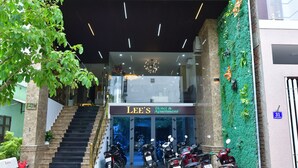 A hotel entrance with a staircase leading to the second floor, a green wall with plants, and several parked motorcycles. - Danang Lee's Studio Apartment near dragon bridge (Đà Nẵng)