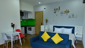 A modern living room with a blue sofa, white table, and red chairs. A kitchen is visible in the background with a green backsplash. - Danang Lee's Studio Apartment near dragon bridge (Đà Nẵng)