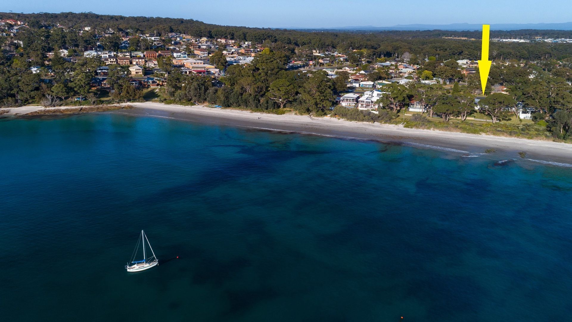 An aerial view of a coastal town with a beach, houses, and a boat.
