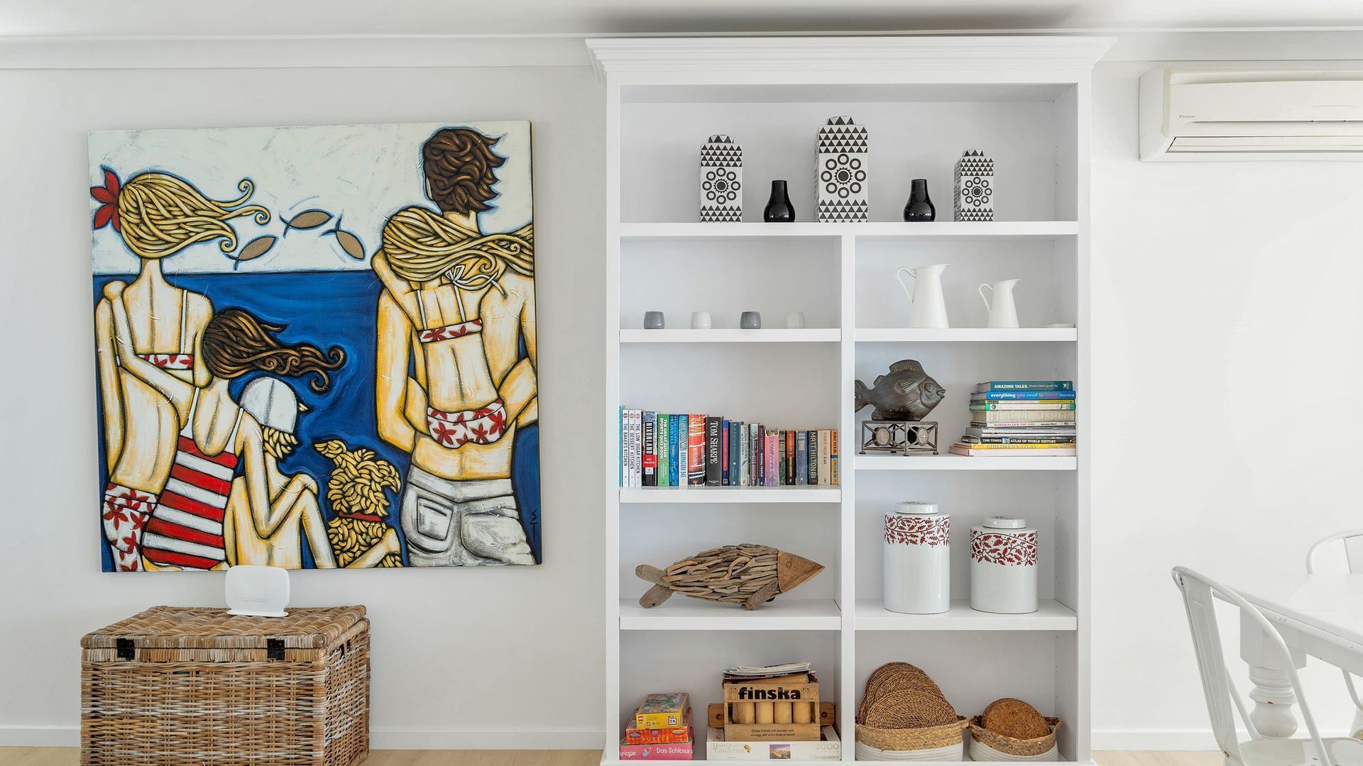 A room with a bookshelf, a painting, and a wicker basket.