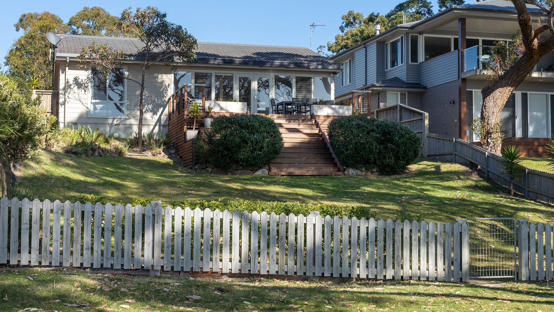 A two-story house with a front porch, a staircase leading to the entrance, and a white picket fence.