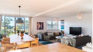 A modern living room with a dining area, large windows, a flat-screen TV, and a cozy seating arrangement. - Palmwood at Hyams Beach (Hyams Beach)