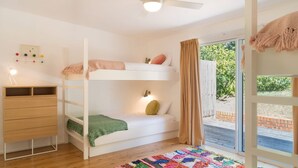 A child's bunk bed with a desk and drawers, a colorful rug, and a view of the outdoors through a glass door. - Palmwood at Hyams Beach (Hyams Beach)