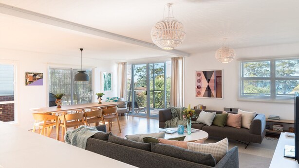 A spacious living area with a dining table, sofas, and a large window offering a view of the outdoors. - Palmwood at Hyams Beach (Hyams Beach)